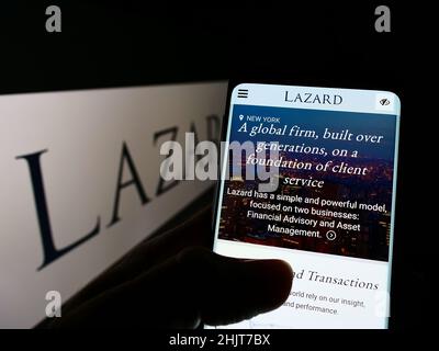 Person, die Mobiltelefon mit der Webseite des US-Finanzdienstleisters Lazard Ltd. Auf dem Bildschirm vor dem Logo hält. Konzentrieren Sie sich auf die Mitte des Telefondisplays. Stockfoto