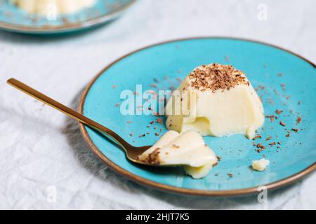 Vanillepudding auf blauem Porzellanteller mit Schokoladenbröseln darauf. Heller Hintergrund Stockfoto