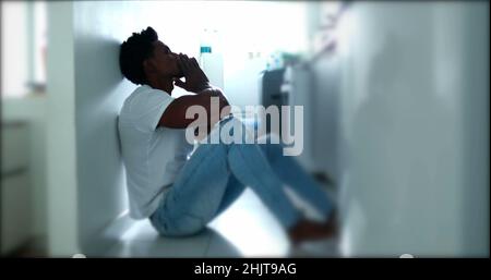 Deprimierter Mann, der auf dem Boden sitzt. Traurige unglückliche Person, die seine Stirn hält und an einer psychischen Erkrankung leidet Stockfoto