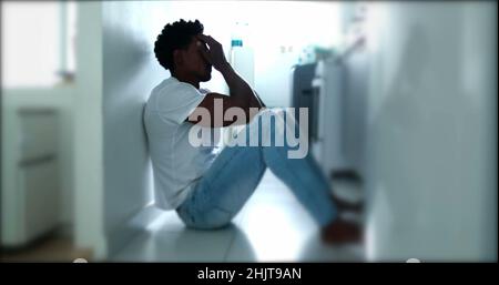 Deprimierter Mann, der auf dem Boden sitzt. Traurige unglückliche Person, die seine Stirn hält und an einer psychischen Erkrankung leidet Stockfoto