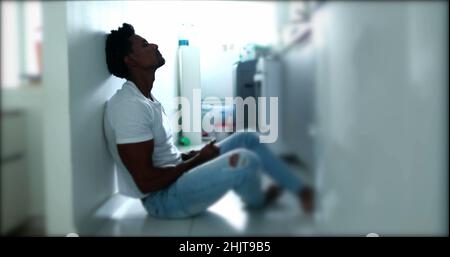 Deprimierter Mann, der auf dem Boden sitzt. Traurige unglückliche Person, die seine Stirn hält und an einer psychischen Erkrankung leidet Stockfoto