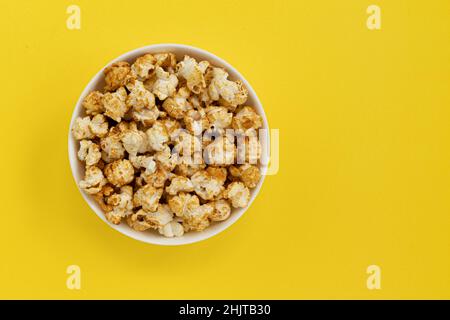 Karamell-Popcorn in einer Schüssel auf Gelb mit Platz für Text, Nahaufnahmen, süße Snacks und Karamell-Popcorn zum Ansehen von Filmen Stockfoto