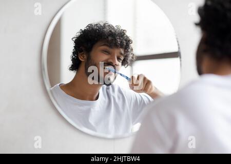 Zahnpflege. Glücklicher inder, der im Badezimmer seine Zähne mit einer Zahnbürste putzt, selektiver Fokus auf Reflexion Stockfoto