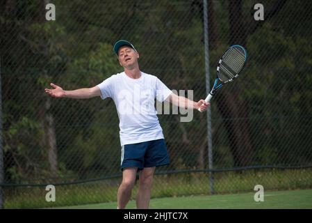Ein Australier in den Fünfzigern oder Sechzigern steht auf einem örtlichen Tennisplatz, bewaffnet, und appelliert nach einer Entscheidung gegen ihn an den Schiedsrichter (Kamera) Stockfoto
