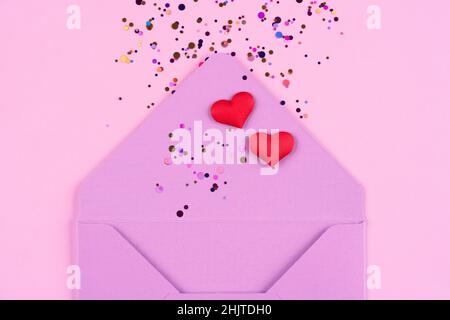 Valentinstag festlichen Hintergrund. Nahaufnahme eines violetten Umschlags mit roten Herzen und Konfetti-Umschlägen auf trendigen rosa Hintergrund mit Kopierraum Stockfoto