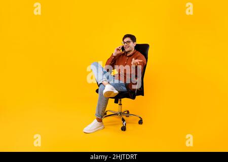 Mann, Der Am Telefon Redet, Sitzt Auf Einem Stuhl Auf Einem Gelben Hintergrund Stockfoto