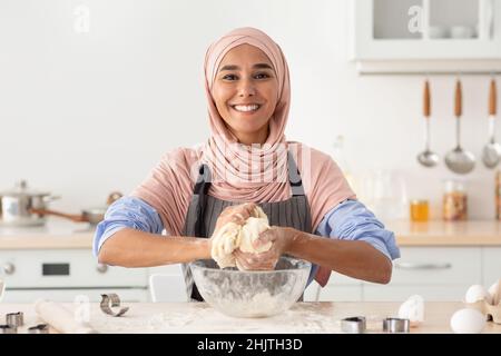 Backen Zu Hause. Glückliche Islamische Frau In Hijab, Die Teig In Der Küche Zubereitet Stockfoto