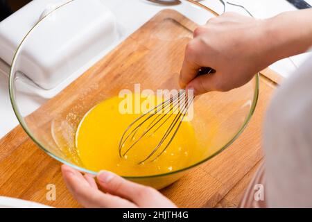 Nahaufnahme der Hände einer Frau, die Eier schlagen, um Teig auf dem Holztisch in der Küche zu machen. Hausgemachte Küche. Stockfoto
