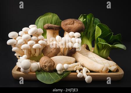 Beliebte ungekochte gesunde asiatische essbare Pilze Buna Shimeji, King Oyster Pilze und Baby Bok Choy auf schwarzem Hintergrund Stockfoto