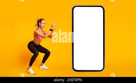 Frau, Die In Der Nähe Des Handyschirms Deep Squats Trainiert, Gelber Hintergrund Stockfoto