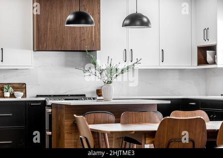 Moderne Küche und Esszimmer im mittleren Jahrhundert mit schwarzen Schränken, weißen Schränken, weißen Quarz- und Walnussakzenten Stockfoto