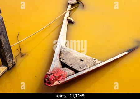 Versunkenes Holzruderboot im verschmutzten Fluss nach einem Sturmschlag. Stockfoto