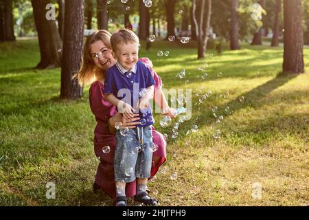 Kind mit Mutter bläst Seifenblase draußen. Stockfoto