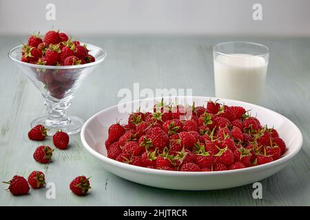 Reife Himbeeren mit Stecklingen auf einem weißen Teller und einem Glas Milch Stockfoto