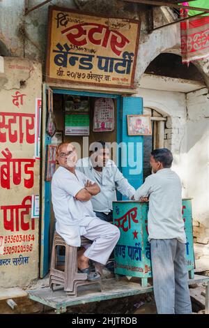 Eine Gruppe von drei Freunden von Männern spricht an einem typischen Kiosk am Straßenrand im Zentrum von Varanasi, einer Stadt am Fluss Ganges in Uttar Pradesh, Nordindien Stockfoto