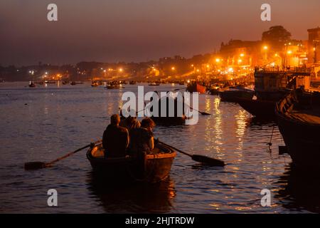 Ruderboote bringen Touristen zur nächtlichen Aarti-Zeremonie auf den Ghats am Fluss Ganges in Varanasi, einer Stadt in Uttar Pradesh, Nordindien Stockfoto