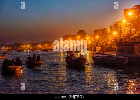 Ruderboote bringen Touristen zur nächtlichen Aarti-Zeremonie auf den Ghats am Fluss Ganges in Varanasi, einer Stadt in Uttar Pradesh, Nordindien Stockfoto