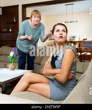 Frau, die während des Streits mit der wütenden Mutter zu Hause sitzt Stockfoto