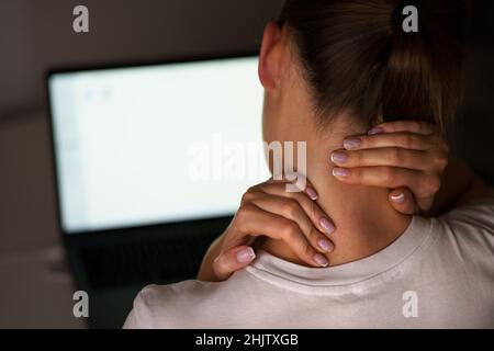 Junge Frau, die nach der Arbeit am Computer an Nackenschmerzen leidet. Massieren Sie den Hals, um Schmerzen zu lindern Stockfoto