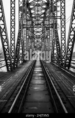 Vertikale Graustufenaufnahme einer langen Metallbrücke über den Fluss Stockfoto