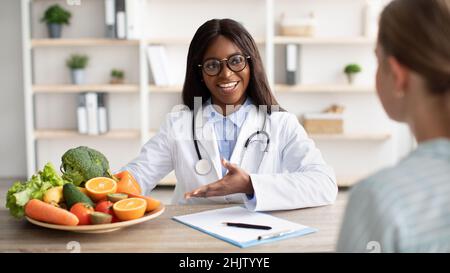 Freundliche Ernährungsberaterin schwarze Frau, die Beratung zu Patienten und Demonstration Teller mit frischem Obst und Gemüse Stockfoto