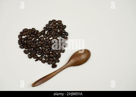 Kaffeebohnen in Herzform und daneben ein Holzlöffel auf bläulich-grauem Hintergrund Stockfoto