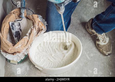 Junge männliche Maler knetet putty mit Wasser in einem Eimer mit einem Handmixer für Gebäude vereint Stockfoto