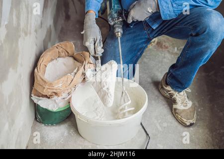 Junge männliche Maler knetet putty mit Wasser in einem Eimer mit einem Handmixer für Gebäude vereint Stockfoto