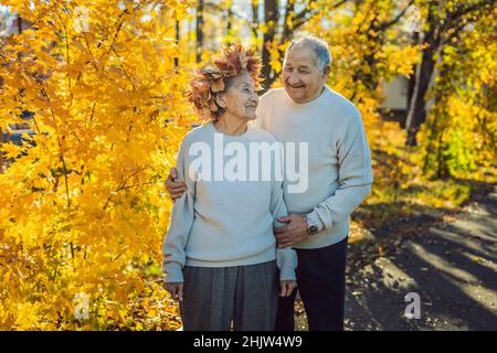 Gerne alte Paar Spaß im Herbst Park. Älterer Mann trägt einen Kranz der Blätter im Herbst zu seiner älteren Frau Stockfoto