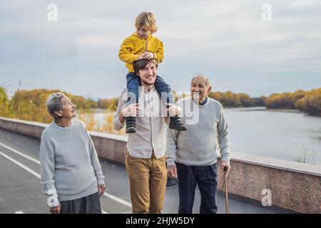 Ein älteres Paar Spaziergänge im Park mit einem Fluss mit ihren Enkel und Urenkel Stockfoto