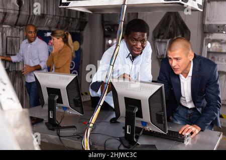 Männer in Panik auf der Suche nach einer Lösung auf dem Computer im Quest-Raum Stockfoto