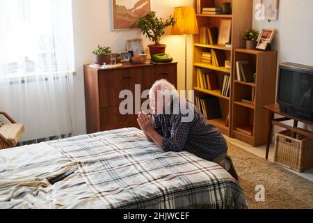 Gealterter Mann legte seine Hände vor das Gesicht, lehnte sich auf das Bett und bete in seinem Schlafzimmer, er dankte Gott für sein Leben Stockfoto