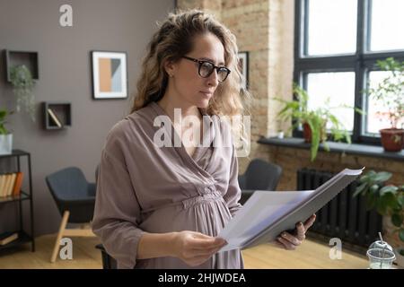 Moderner Buchhalter in eleganter Kleidung, der in Büroumgebungen vor der Kamera durch die Finanzpapiere schaut Stockfoto