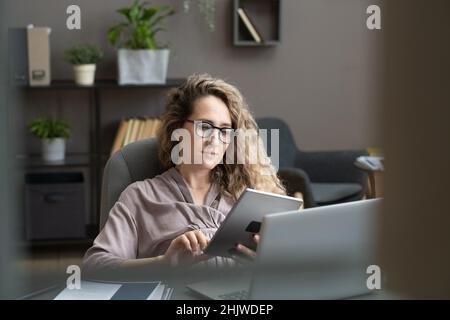 Schwanger blonde Geschäftsfrau sitzt am Arbeitsplatz im Büro und scrollt durch Online-Daten in digitalen Tablet Stockfoto