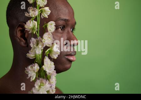 Seitenansicht des Kopfes eines schwarzen Mannes mit weißen Blumen, die nach vorne schauen, während er vor der Kamera auf grünem Hintergrund steht Stockfoto