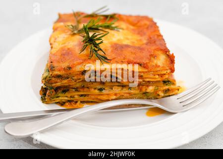 Spinatlasagne. Köstliche Spinatlasagne mit frischem Rosmarin aus nächster Nähe auf einem Teller auf hellgrauem Hintergrund Stockfoto