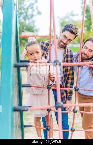 Mädchen auf dem Spielplatz mit ihren Eltern, die unglücklich auf die Kamera schauen. Stockfoto