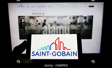 Person, die Mobiltelefon mit Logo der französischen Compagnie de Saint-Gobain S.A. auf dem Bildschirm vor der Geschäftswebseite hält. Konzentrieren Sie sich auf die Telefonanzeige. Stockfoto