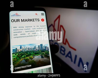 Person, die Mobiltelefon mit der Website der französischen Compagnie de Saint-Gobain SA auf dem Bildschirm vor dem Logo hält. Konzentrieren Sie sich auf die Mitte des Telefondisplays. Stockfoto