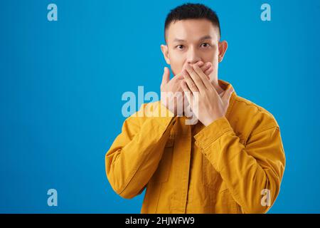 Schockiert aufgeregt jungen Mann den Mund mit beiden Händen und Blick auf die Kamera Stockfoto