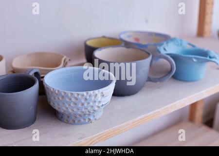 Leeres handgemachtes Geschirr. Keramikbecher auf dem Regal. Handarbeit. Glasur von blauer Farbe auf Ton Stockfoto