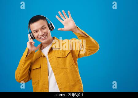 Fröhlicher junger Mann mit Kopfhörern, der Musik hört und mit der Hand winkt Stockfoto
