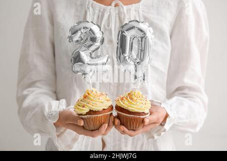 Frau hält Geburtstagskuchen mit der Nummer 20 auf hellem Hintergrund Stockfoto