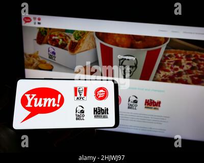 Person mit Mobiltelefon und Logo des amerikanischen Fast-Food-Unternehmens Yum! Brands Inc. Auf dem Bildschirm vor der Webseite. Konzentrieren Sie sich auf die Telefonanzeige. Stockfoto