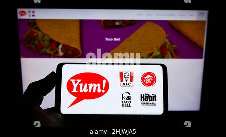 Person mit Mobiltelefon und Logo des US-amerikanischen Fast-Food-Unternehmens Yum! Brands Inc. Auf dem Bildschirm vor der Business-Webseite. Konzentrieren Sie sich auf die Telefonanzeige. Stockfoto