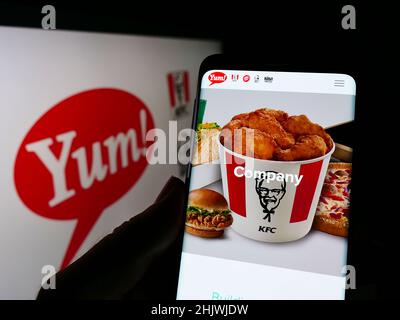 Person mit Mobiltelefon auf der Website des US-amerikanischen Fast-Food-Unternehmens Yum! Brands Inc. Auf dem Bildschirm vor dem Logo. Konzentrieren Sie sich auf die Mitte des Telefondisplays. Stockfoto