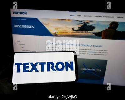 Person mit Mobiltelefon und Logo des US-Luftfahrtunternehmens Textron Inc. Auf dem Bildschirm vor der Business-Webseite. Konzentrieren Sie sich auf die Telefonanzeige. Stockfoto