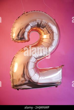 Berlin, Deutschland. 14th Januar 2022. ABBILDUNG - Ein goldener Ballon in Form der Zahl 2 hängt vor einem rosa Hintergrund. (Posierte Szene) die '2': Symbol für Gegensätze, aber auch für romantische Liebe. Für einige ist es eine glückliche Zahl, für andere nur eine von zehn Ziffern. Sie ist allgegenwärtig. (To dpa: 'Die Nummer zwei: Mathematisch, gesellig, rückwärts') Quelle: Annette Riedl/dpa/Alamy Live News Stockfoto