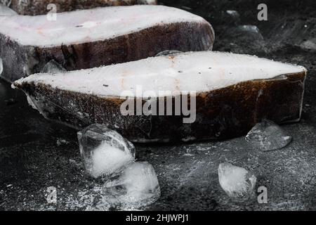 Gefrorene Filets von weißen Fischen, pollock-Set, auf schwarzem dunklen Stein-Tischhintergrund, mit Platz für Text Stockfoto