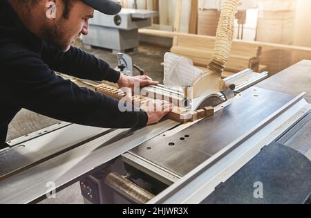 Zugeschnittenes Bild eines erfahrenen Handwerkers, der in einer Werkstatt mit einer Kreissäge eine Holzdiele schneidet. Horizontale Aufnahme Stockfoto